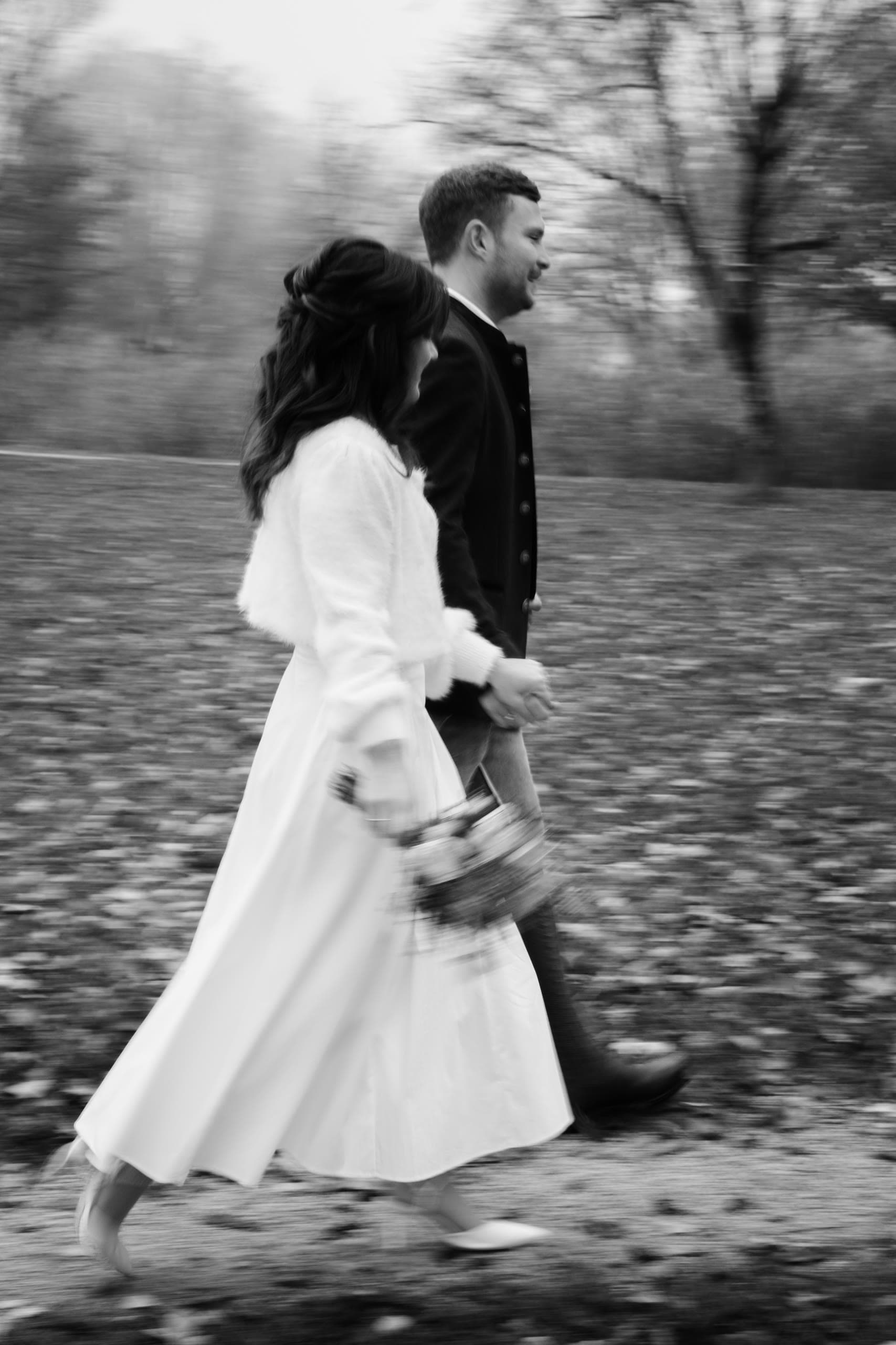 Couple walk briskly hand in hand across a leaf-strewn path, motion blurred, black and white