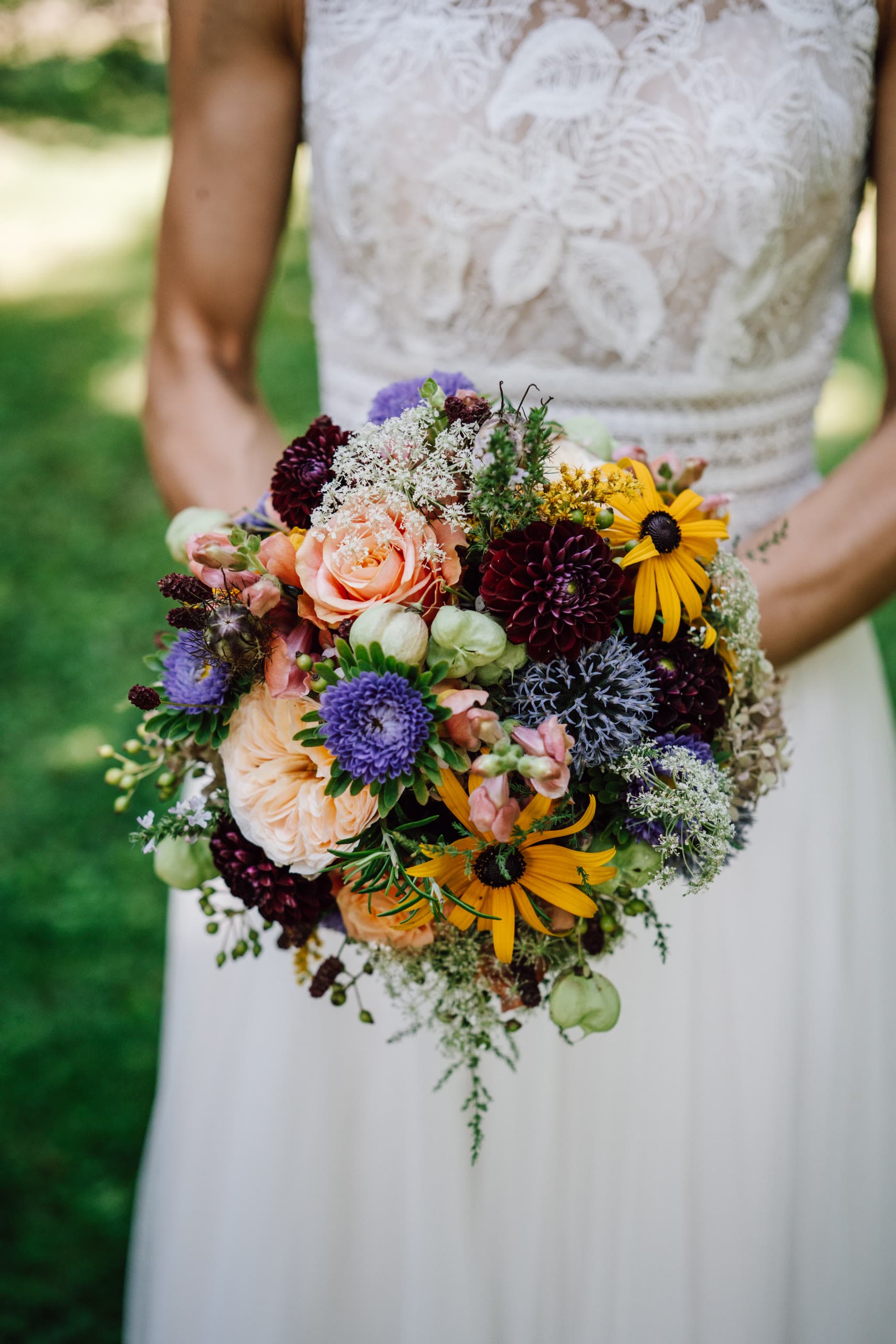 Bride holds a bouquet of peach roses, purple asters and yellow black-eyed susans