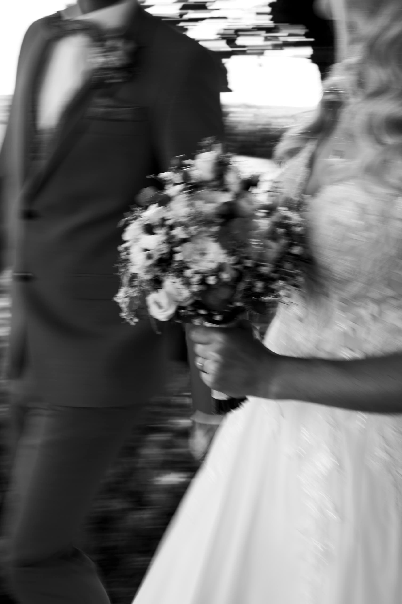 Motion-blurred close-up of the bride's bouquet against the groom's dark suit, black and white