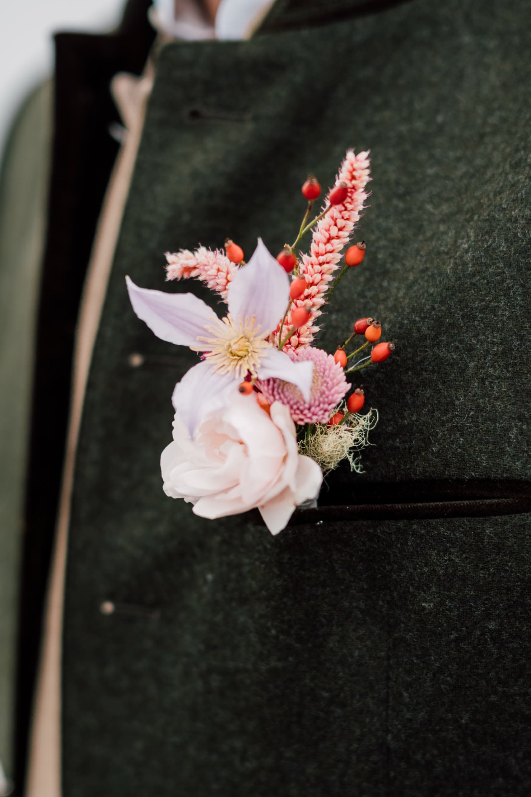 Close-up of a boutonniere with a pink flower and red berries on a green jacket
