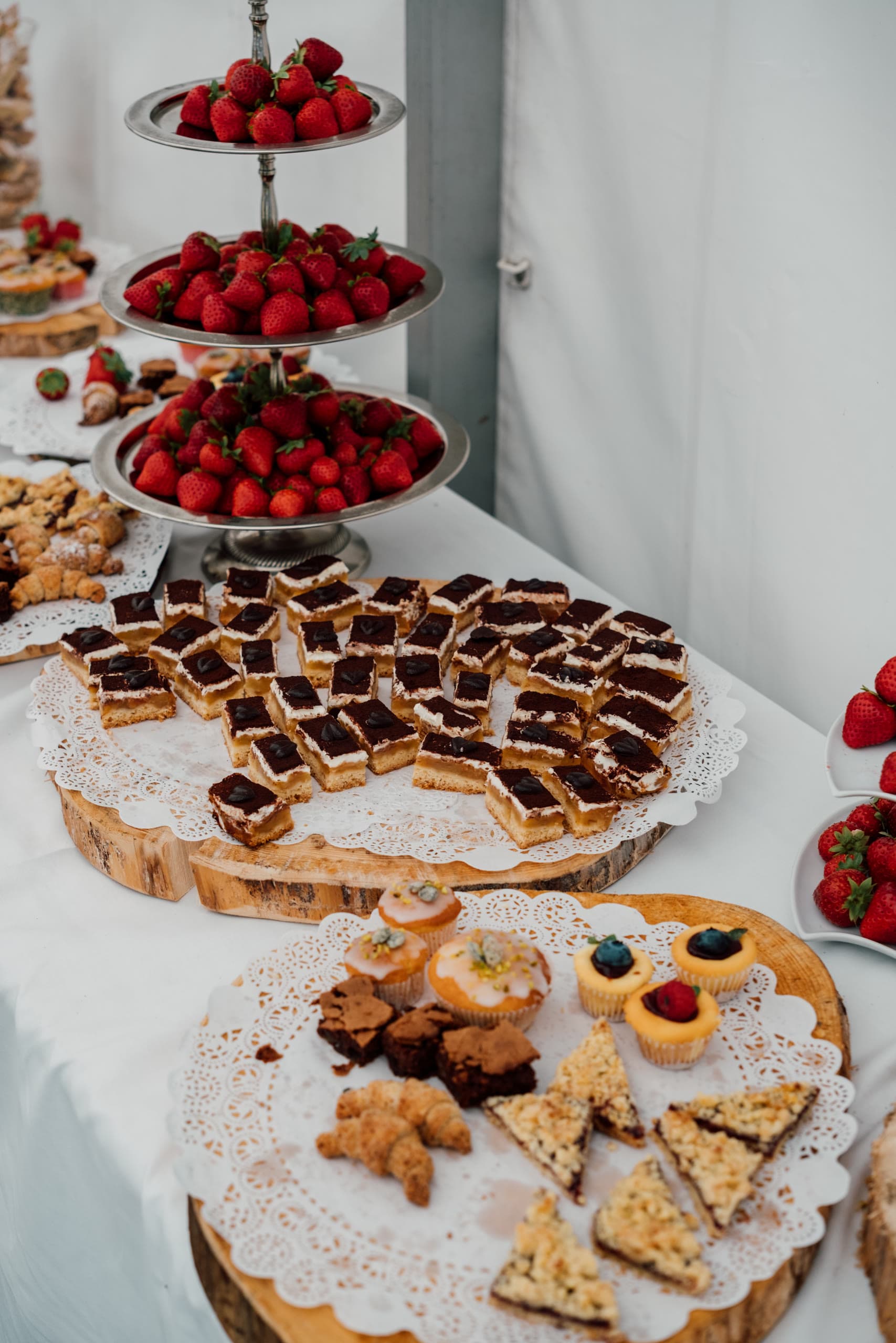 Three-tier stand of strawberries beside trays of pastries on a table