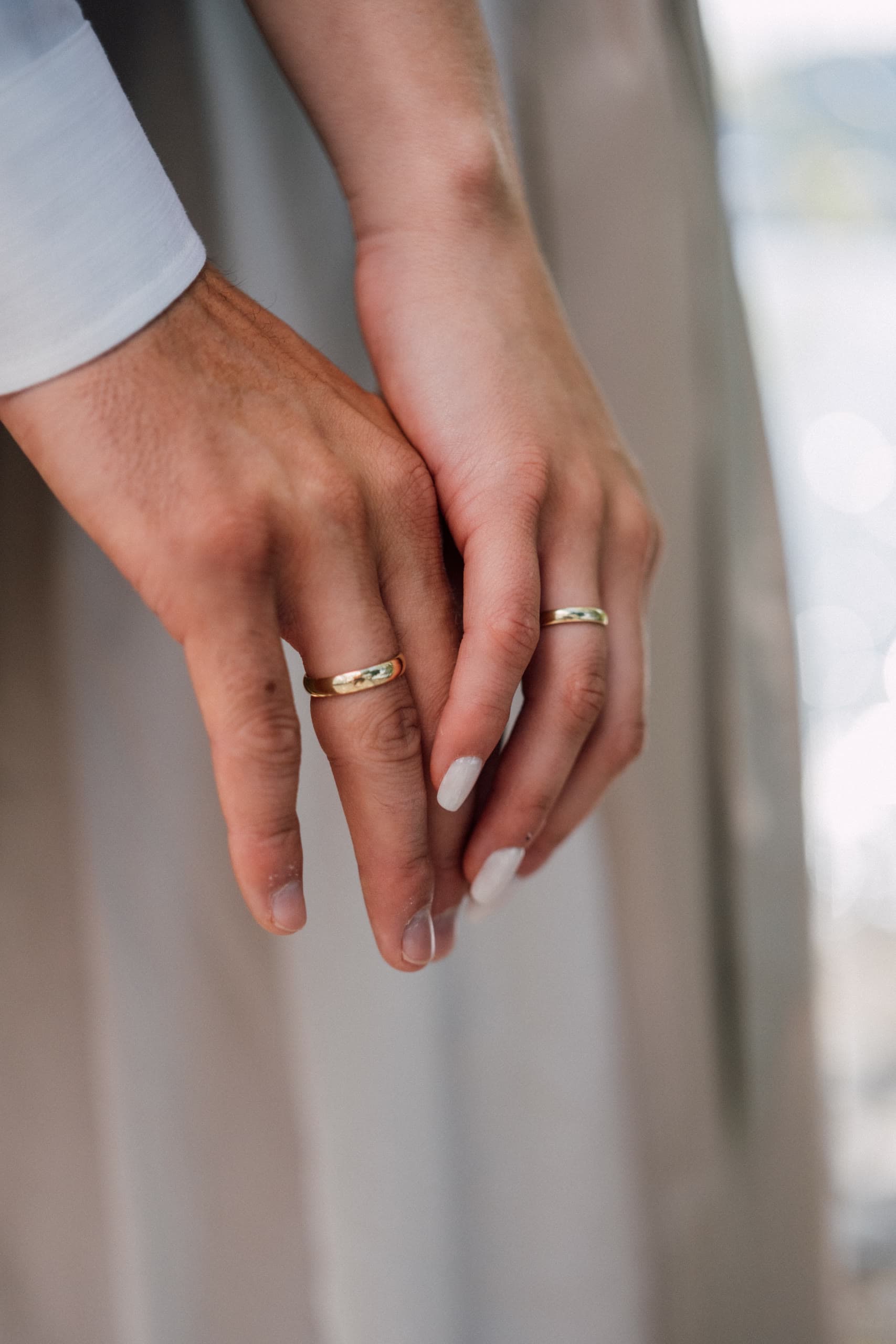Close-up of clasped hands wearing gold wedding rings against a soft fabric background