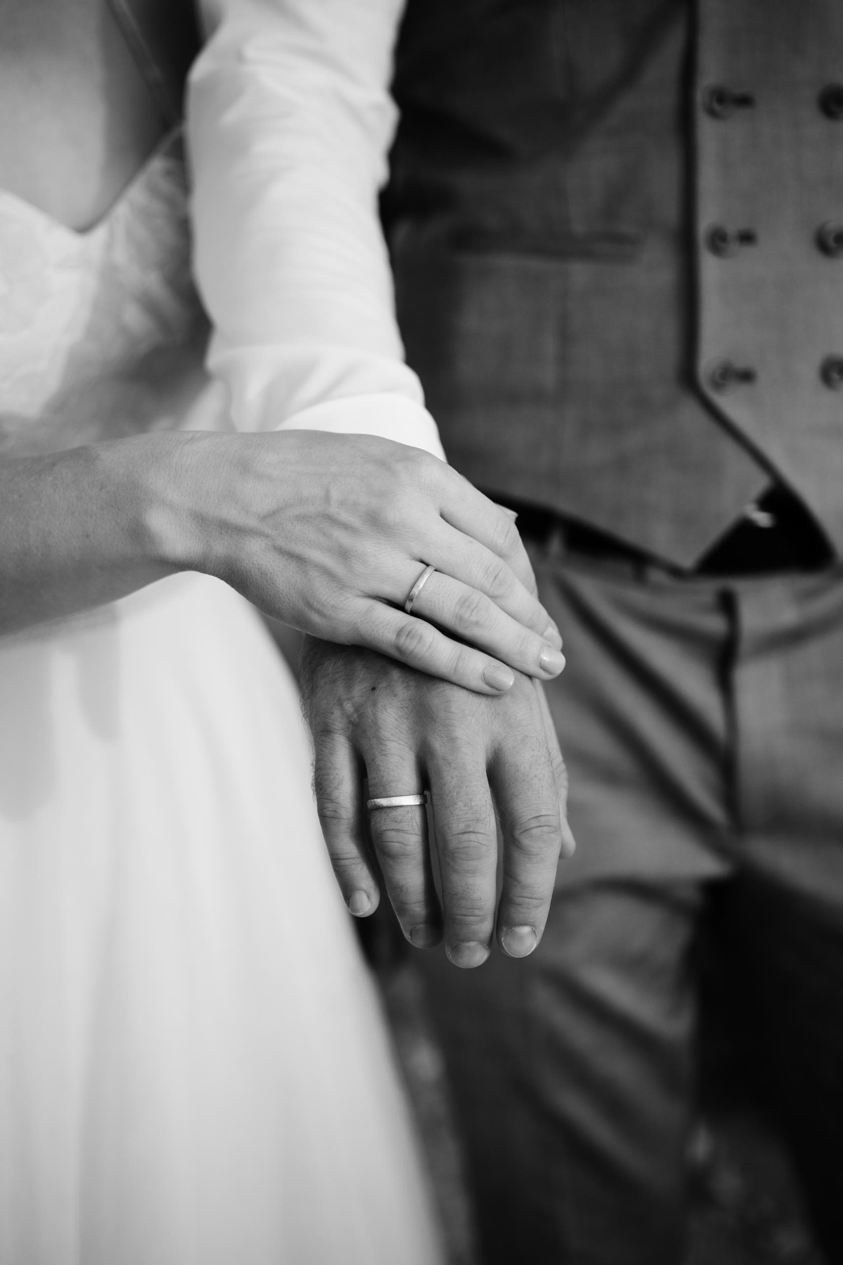 Black and white close-up of the bride's hand resting on the groom's, both wearing rings