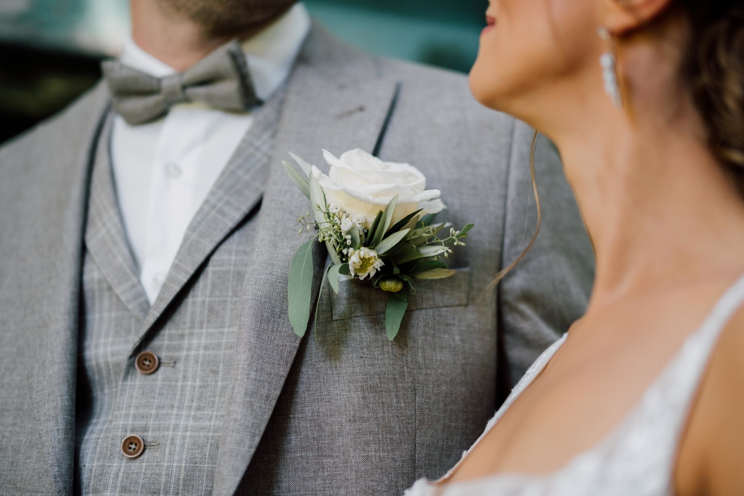 Close-up of a white rose boutonniere with olive leaves on a grey checked waistcoat