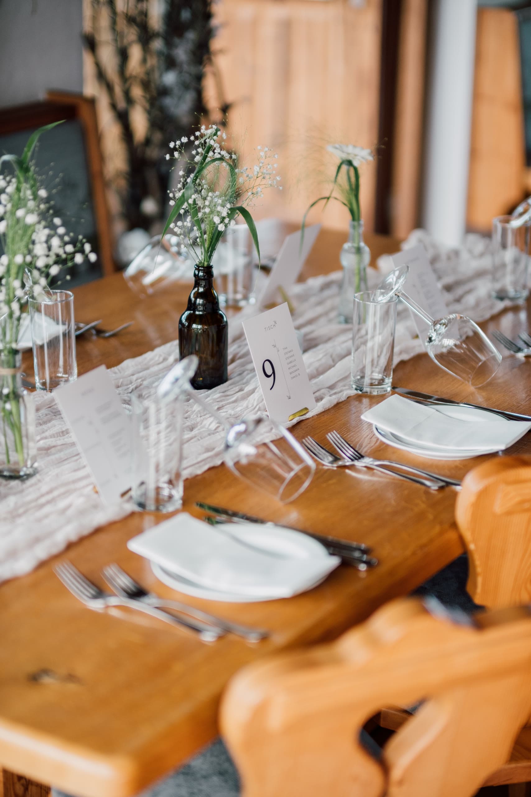Wooden table set with plates, cutlery, wine glasses, small white flowers and a place card