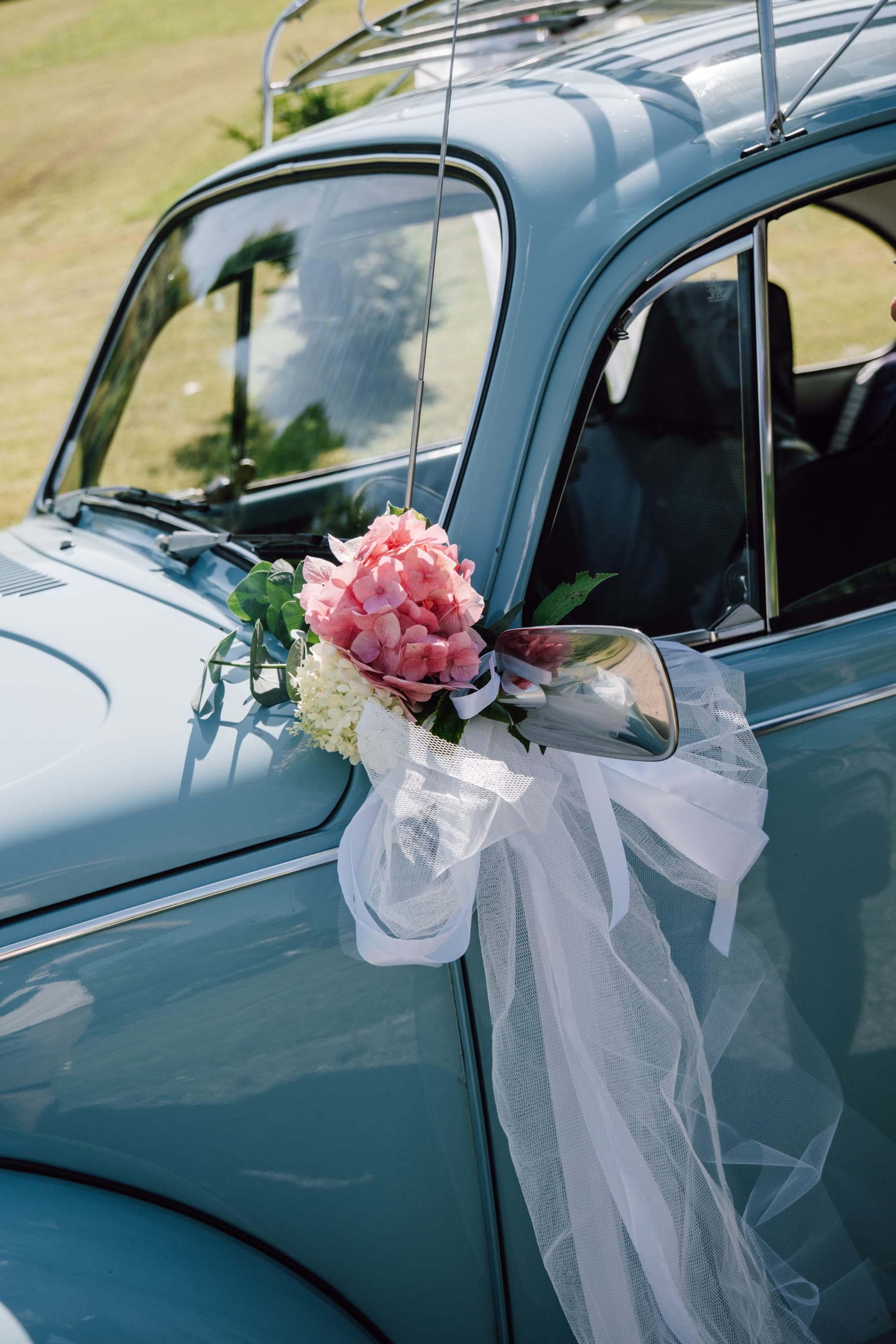 Pink and white flower posy with tulle ribbon tied to the wing mirror of a vintage blue car