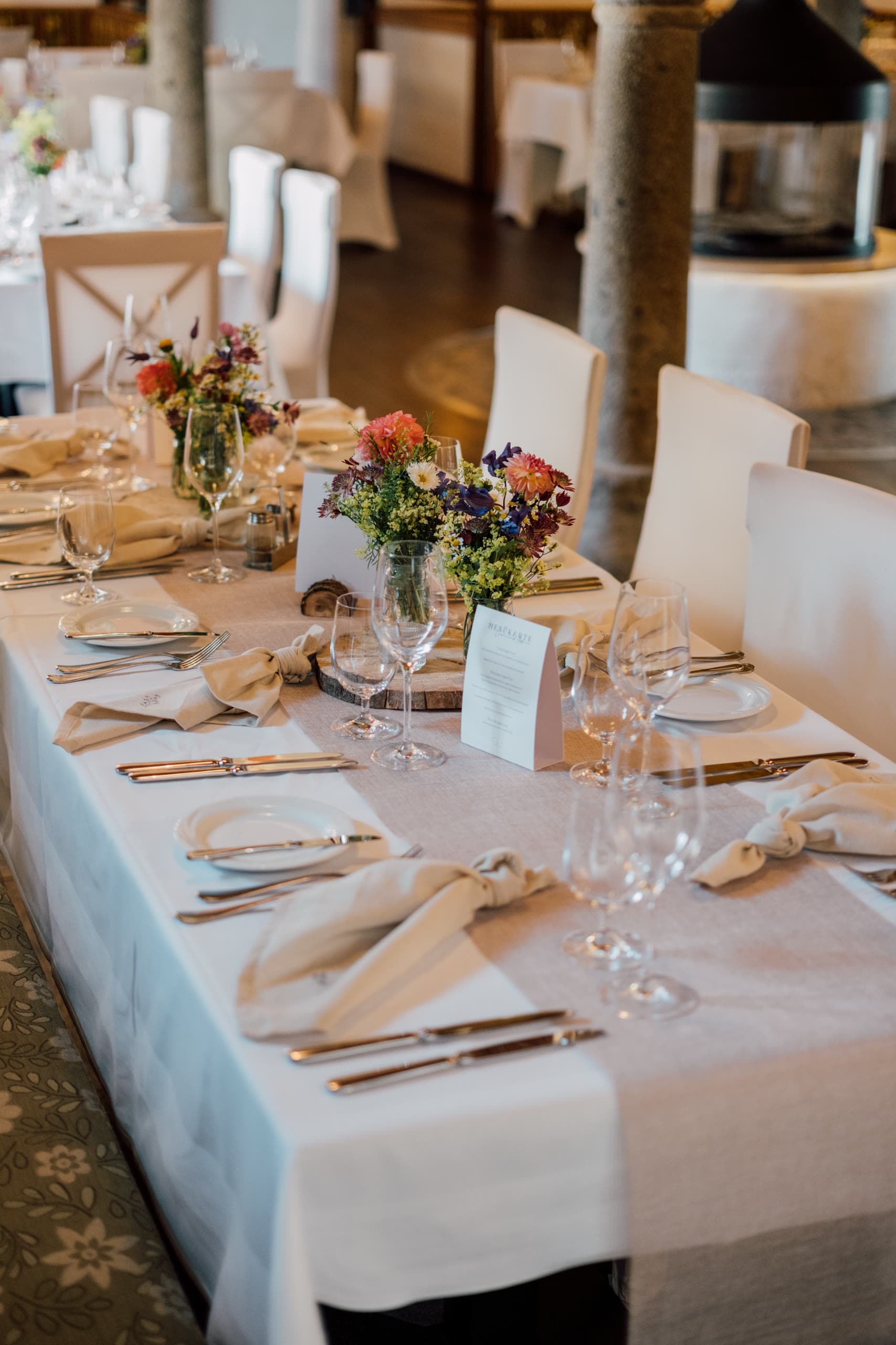 Long reception table set with white linen, wine glasses and colourful flower centrepieces