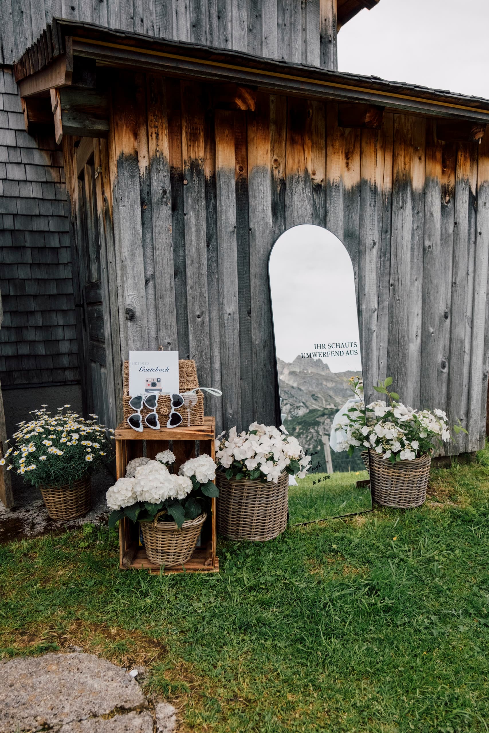 Wicker baskets of white hydrangea and daisies beside a mirror against a wooden barn wall