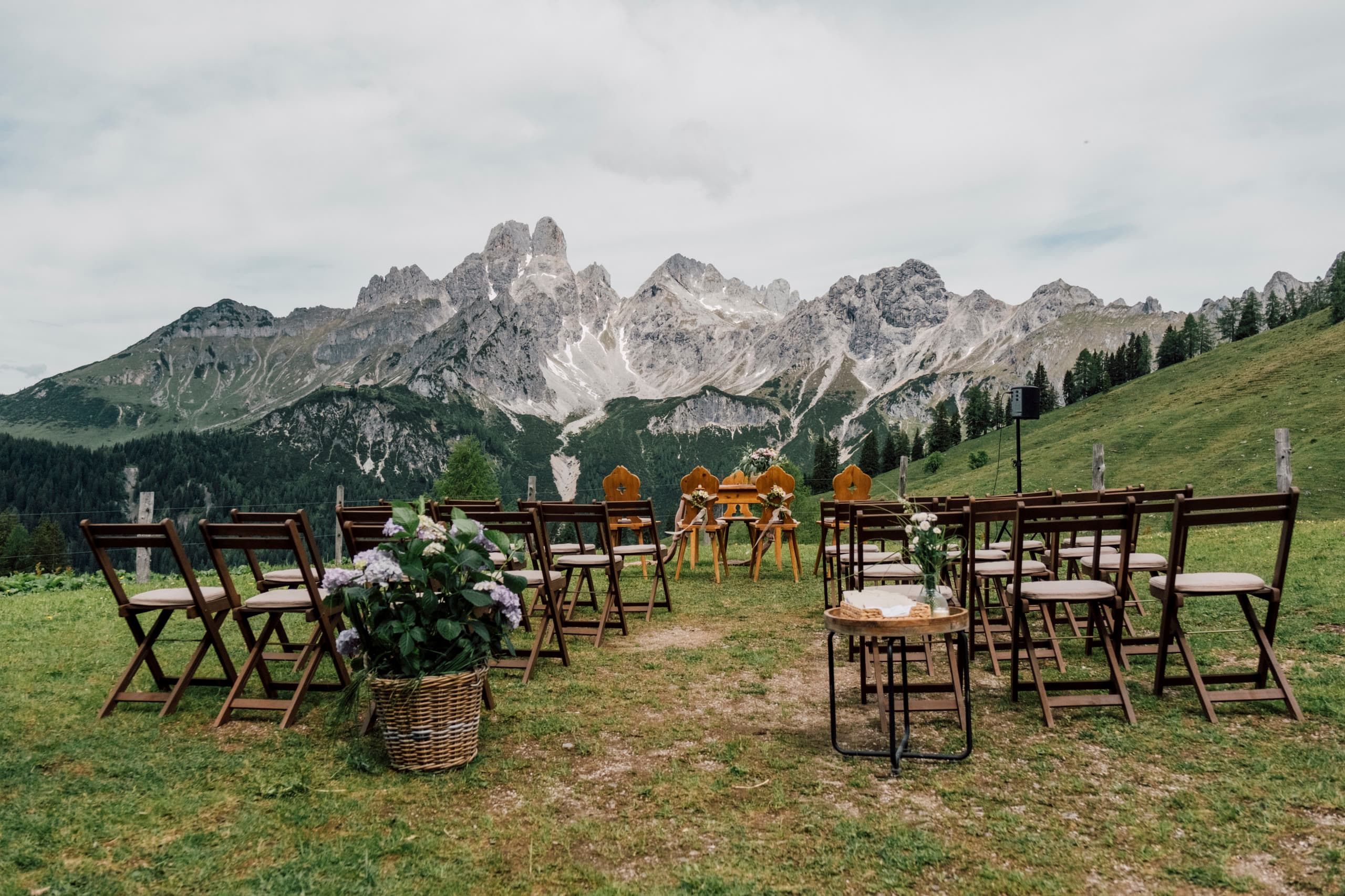 Rows of empty wooden chairs set for an outdoor ceremony facing grey mountain peaks